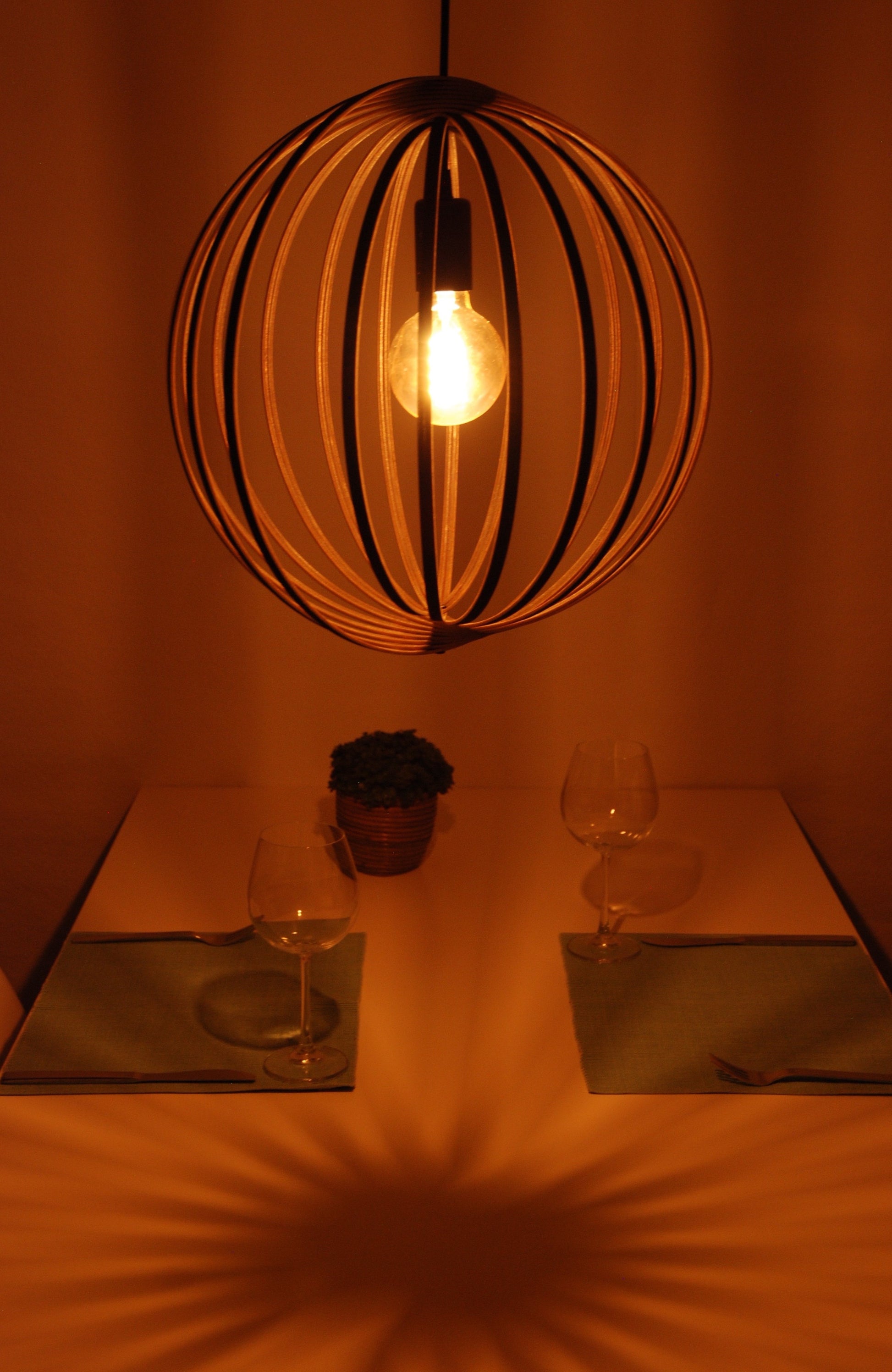 LUWALD NO.03 M Pendelleuchte aus Holz, schwarz, handgefertigt, kugelförmig, angeschaltet, Tisch mit Deko, gemütlich